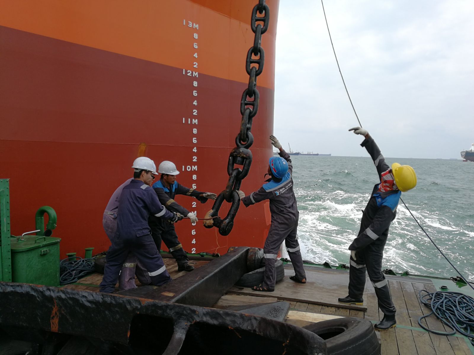 Crew handling mooring chains alongside a vessel at sea