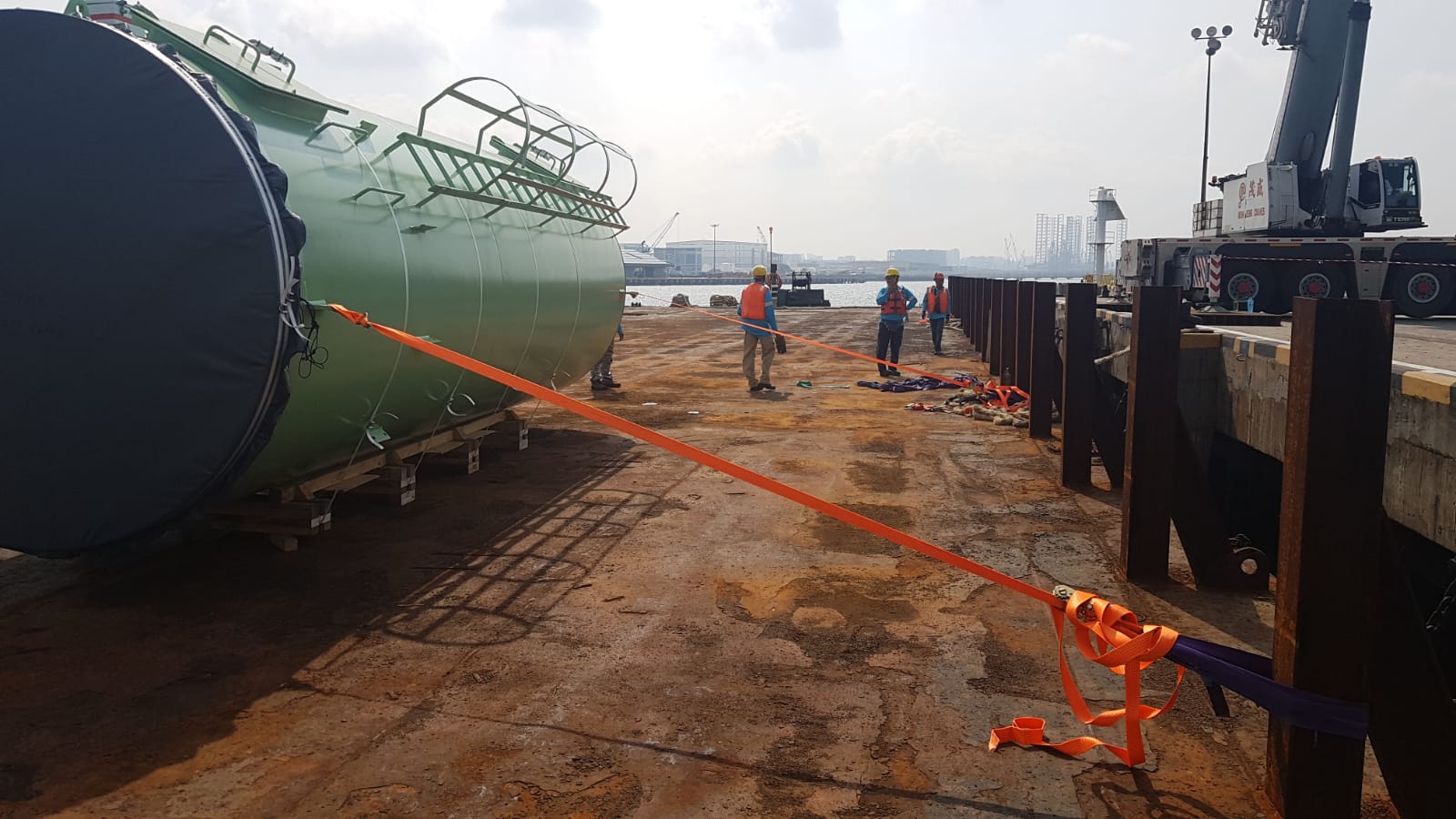 Riggers moving an oversized green pressure vessel on a wharf